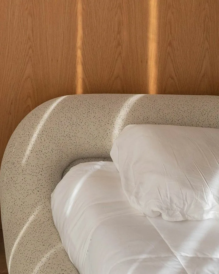 Gemachtes Hotelbett mit weißer Bettwäsche vor einer warmen Holzwand